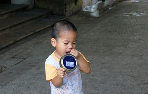 Một cậu bé thơ thẩn trong sân và tìm cách vét lại những gì còn bỏ sót trong hộp thịt