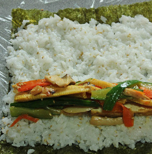 Rải đều cơm l&ecirc;n mặt rong biển, lần lượt cho rau l&ecirc;n rồi cuộn chặn
