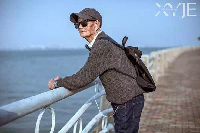 Cụ ông ngắm biển trong trang phục mũ lưỡi trai, kính râm, quần jeans kết hợp áo sơ mi như một thanh niên thời thượng.
