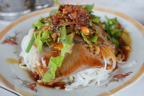Hủ tiếu mà được bày trong… đĩa, thật làm người ta hiếu kỳ. Đây là một loại hủ tiếu đặc biệt của vùng Sa Đéc, một trong những đặc sản Cần Thơ. Những cọng hủ tiếu tươi to, trắng ngà bày lên đĩa, bên trên là tim, gan, thịt heo thái. Thêm chút hẹ, xà lách tươi xắt nhuyễn và hành phi càng tăng sự hấp dẫn cho món ăn. Điểm nhấn đáng chú ý nhất là nước sốt màu vàng đậm rưới trên cùng đĩa hủ tiếu. Đó là bí quyết làm nên vị khác lạ, ngon lành khi ăn. Để người ăn không cảm thấy khô, đĩa hủ tiếu được phục vụ kèm chén nước dùng nếu khách thích.