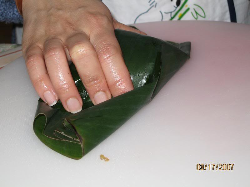 M&uacute;c một &iacute;t bột cho v&agrave;o kế l&agrave; cho nh&acirc;n, cho trứng c&uacute;t v&agrave;o, cho 1 muỗng nh&acirc;n l&ecirc;n. Rồi lại cho một muỗng bột l&ecirc;n tr&ecirc;n c&ugrave;ng, miết đều ra cho bột che hết thịt. Lấy 1 miếng l&aacute; chuối đậy l&ecirc;n tr&ecirc;n mặt bột.