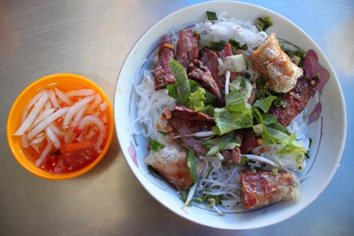 L&uacute;c ăn, xếp rau x&agrave; l&aacute;ch đ&atilde; th&aacute;i nhỏ xuống dưới b&aacute;t, b&ecirc;n tr&ecirc;n để b&uacute;n, thịt nướng, c&agrave; rốt v&agrave; rắc &iacute;t đậu phộng l&ecirc;n bề mặt thịt. Chan nước mắm chua ngọt, trộn đều l&ecirc;n.