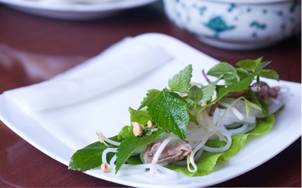 Trải 1 tấm b&aacute;nh phở l&ecirc;n đĩa. Xếp x&agrave; l&aacute;ch (rau diếp), ch&uacute;t b&uacute;n, thịt b&ograve; x&agrave;o, v&agrave;i cọng rau sống mỗi loại, cuối c&ugrave;ng rắc &iacute;t lạc v&agrave; h&agrave;nh t&iacute;m phi, cuốn chặt.