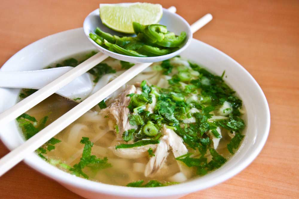 Xếp b&aacute;nh phở ra t&ocirc;, cho thịt g&agrave; x&eacute;, h&agrave;nh t&acirc;y, rau răm, một &iacute;t ti&ecirc;u v&agrave; chan nước d&ugrave;ng v&agrave;o d&ugrave;ng n&oacute;ng.