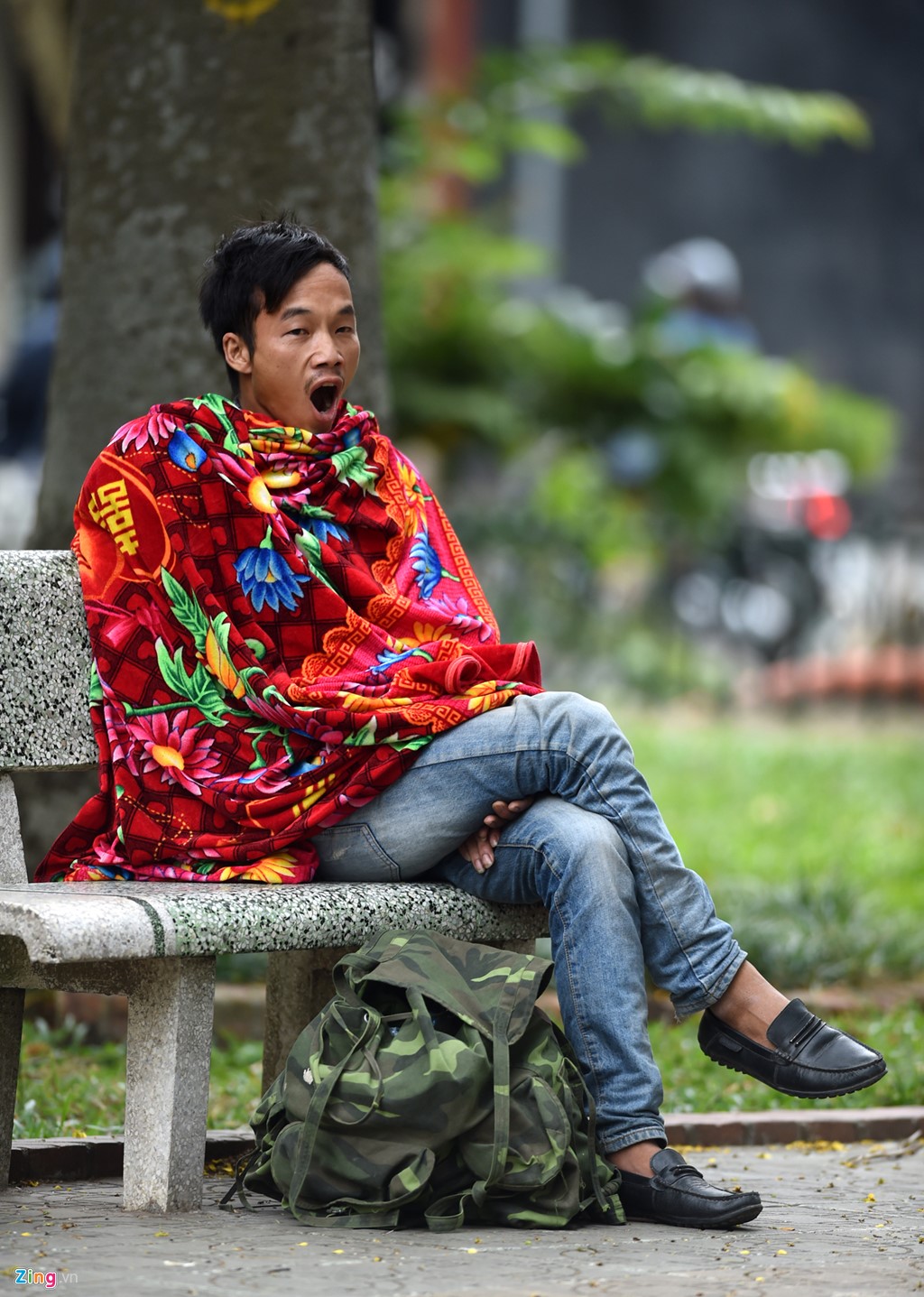 Một người đàn ông quấn chiếc chăn quanh mình ngồi ghế đá vườn hoa Quán Sứ. Thời tiết thay đổi khiến anh không kịp thích nghi, ngáp ngủ liên tục. Ảnh: Tri thức trực tuyến 