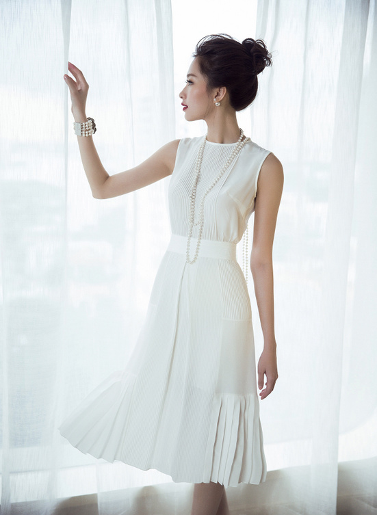 Cũng với sắc trắng, nhưng trong set đồ thuần trắng với đầm bằng lụa sát nách nhấn ở phần eo phối cùng vòng cổ ngọc trai dáng dài…