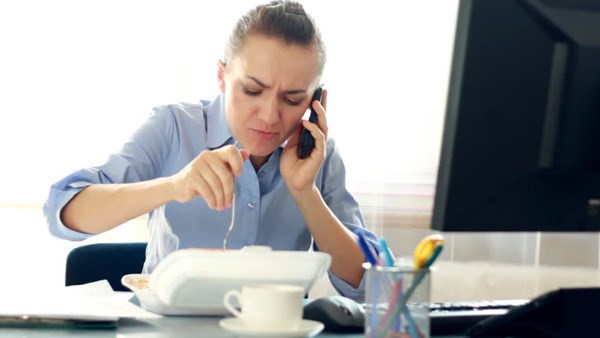 Ăn trưa tại b&agrave;n l&agrave;m việc l&agrave; th&oacute;i quen nhiều người mắc. Ảnh minh họa 