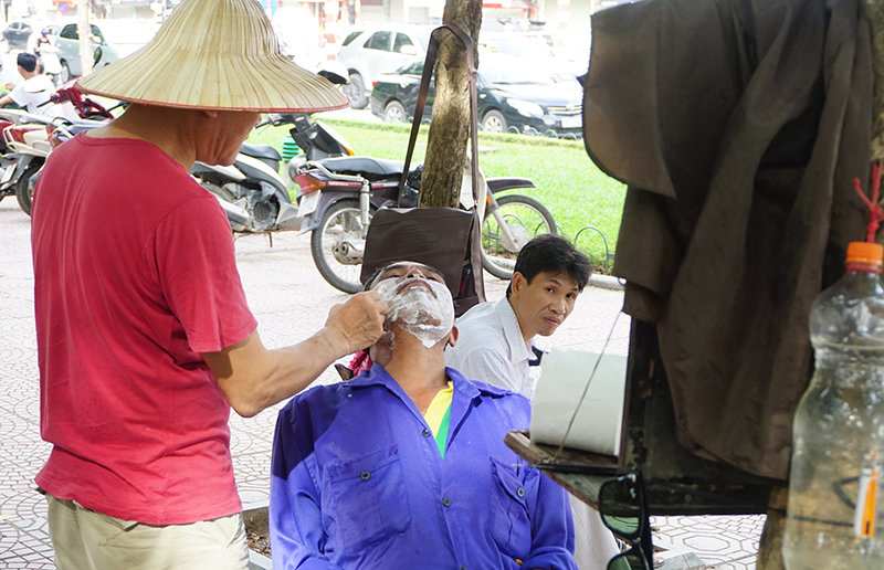 Một phụ huynh đến từ huyện Thanh Oai tranh thủ cắt tóc, cạo râu trong lúc chờ con đi thi. Ảnh Dân Trí