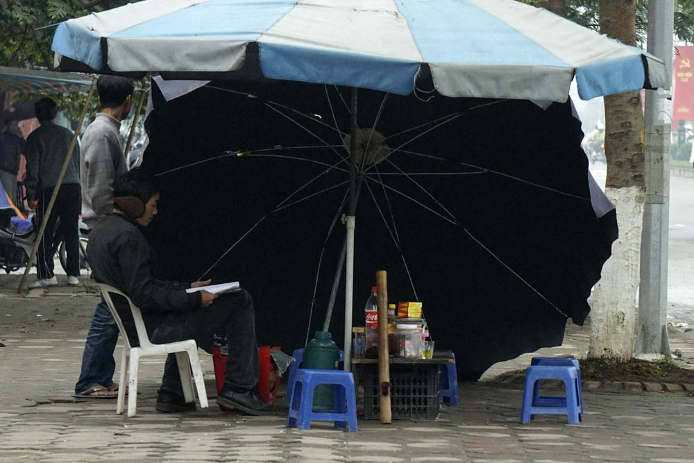 Một quán cóc ven đường nghiêng ô không để che nắng mà để chắn đợt gió mùa ào ạt thổi. Ảnh: Dân Trí