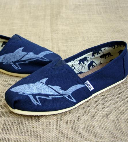 Giày Toms in họa tiết cá mập: Đôi giày với họa tiết cá mập được in thủ công màu trắng nổi bật trên nền vải canvas sắc xanh dương này sẽ giúp bạn trông vô cùng khỏe khoắn và phong cách. Chúng có giá $85 trên trang scoutmob.com.