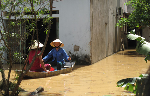 Hai phụ nữ trong  v&ugrave;ng lũ ở Thanh H&oacute;a phải d&ugrave;ng thuyền di chuyển v&agrave;o nh&agrave; v&igrave; c&aacute;c con đường bộ đều bị ngập s&acirc;u