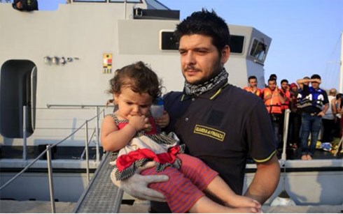 Cảnh s&aacute;t biển Italia bế một em b&eacute; tỵ nạn người Syria cập b&atilde;i biển Hy Lạp ng&agrave;y 10/8 